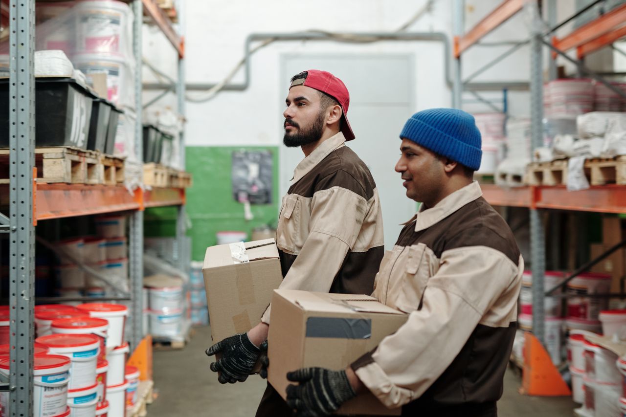 Two warehouse workers carrying cartons between racking